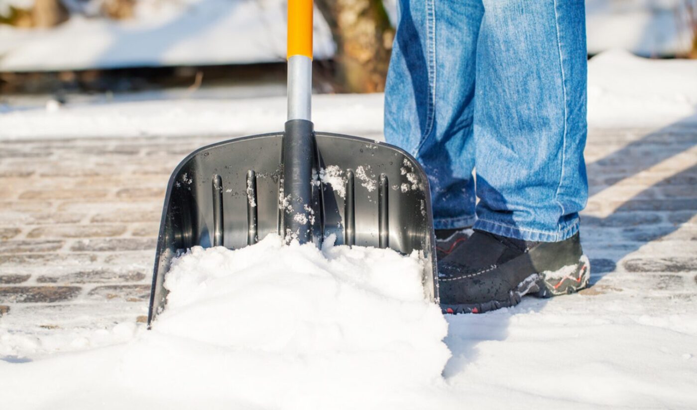 Людина прибирає сніг великою чорною лопатою на подвір'ї