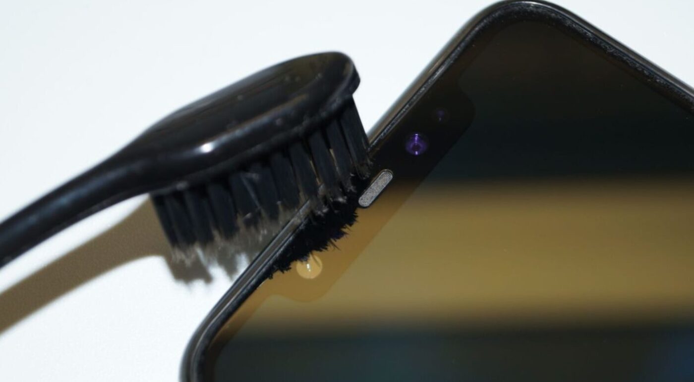 Процес чищення динаміка смартфона зубною щіткою від пилу